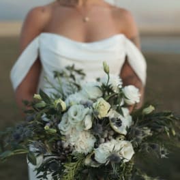 Bride holding a white and green bouquet with roses and thistle