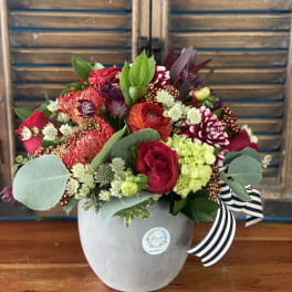 Mixed red and pink flower arrangement in a gray vase with a striped ribbon