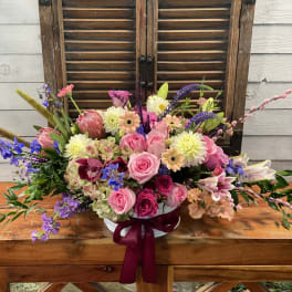 Mixed pink and purple flower arrangement in a white vase with ribbon