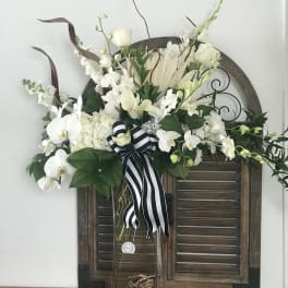 White orchid and rose arrangement in a tall glass vase with a striped ribbon