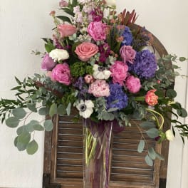 Mixed bouquet of pink, purple, and white flowers in a tall clear vase