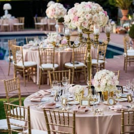 Blush and white rose centerpieces on gold stands at an outdoor table setting.