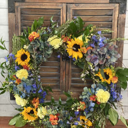Floral wreath with sunflowers, blue blooms, and yellow carnations on a wooden shutter