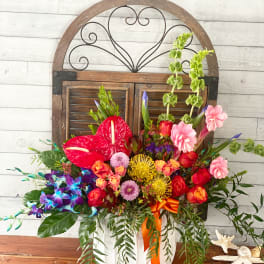 Colorful mixed flower arrangement in a white container with an orange ribbon