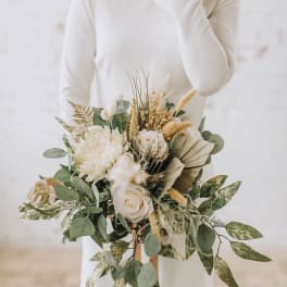 Bride holding a cream and green bouquet with roses and dried grasses