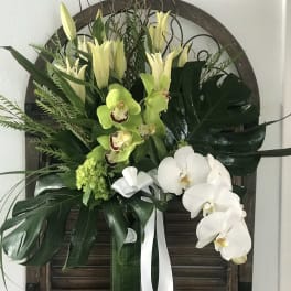 Tall floral arrangement with white orchids and green lilies in a vase