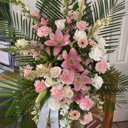 Pink and white floral standing spray with palm fronds and a white ribbon