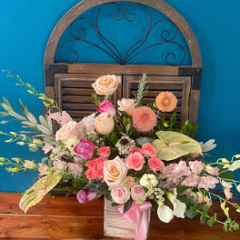 Mixed pink and peach floral arrangement in a wooden box with a pink ribbon