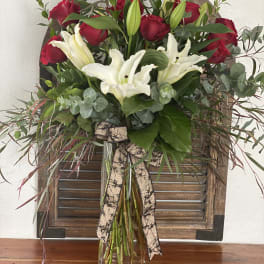 Red roses and white lilies in a clear glass vase with a ribbon