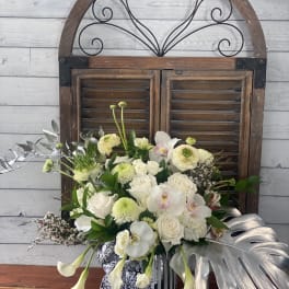 White and pale green floral arrangement in a striped vase with silver leaves