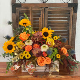 Mixed bouquet with sunflowers, orange roses, and orchids in a wooden container