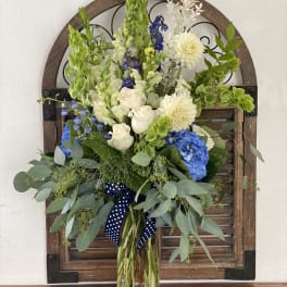 Tall bouquet of white, blue, and green flowers in a glass vase