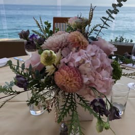 Pastel floral centerpiece in a low square vase on a table by the water