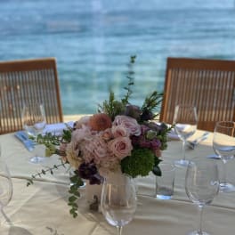 Pastel floral centerpiece in a white vase on a set dining table by the water