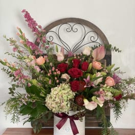 Mixed bouquet of roses, lilies, and hydrangea in a white vase with a ribbon