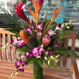 Tropical arrangement with purple orchids, red ginger, and orange heliconia in a tall vase