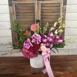 Pink and purple floral arrangement in a white vase with a pink ribbon