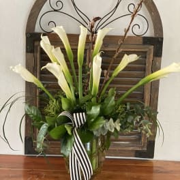 White calla lilies in a glass vase with a striped ribbon