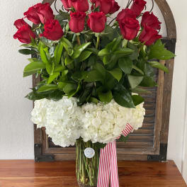 Red roses above white hydrangeas in a glass vase with a striped ribbon