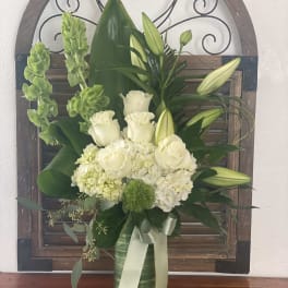 White roses and lilies arranged in a green vase with a ribbon