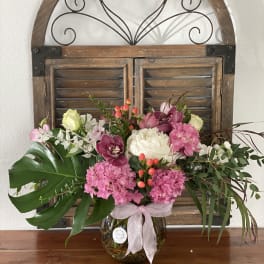 Pink and white floral arrangement in a glass vase with a ribbon