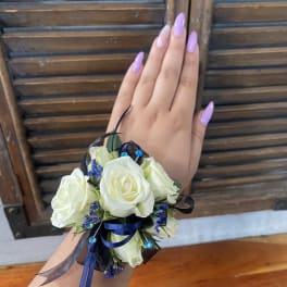 White rose wrist corsage with blue ribbon and small purple accents
