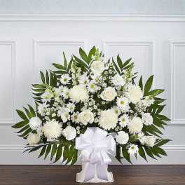 White floral spray with daisies and roses in a white stand with ribbon