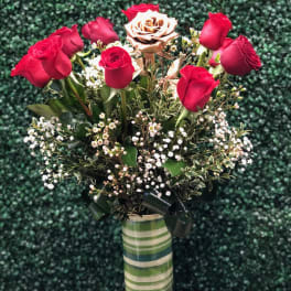 Tall vase of red roses with a single gold rose and white filler flowers in a striped green vase