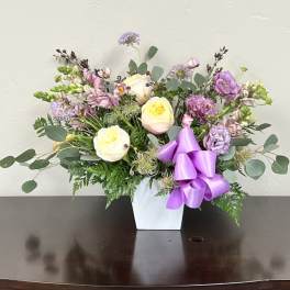 Pastel floral arrangement in a white vase with a purple ribbon