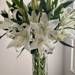 White lilies arranged in a tall clear glass vase
