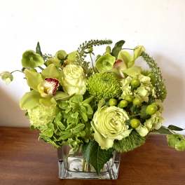 Green floral arrangement in a clear square vase