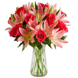 Pink lilies and red roses arranged in a clear glass vase