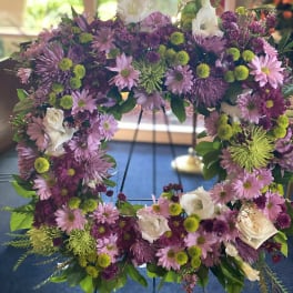 Purple and pink floral wreath with white roses on a stand