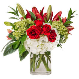 Red roses, red lilies, and white hydrangeas arranged in a clear glass cylinder vase