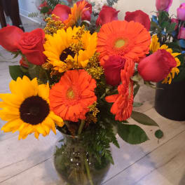 Mixed bouquet of sunflowers, gerbera daisies, and red roses in a glass vase