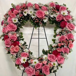 Heart-shaped floral wreath with pink roses and white daisies on a stand