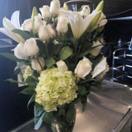 White lilies and roses in a glass vase with a pale green hydrangea bloom