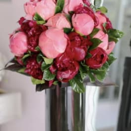 Round bouquet of pink and dark red peonies in a tall dark glass vase