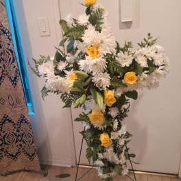 Cross-shaped floral spray with white daisies and yellow roses on a stand
