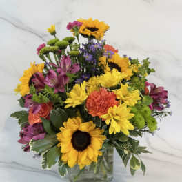 Bright mixed bouquet with sunflowers, daisies, and alstroemeria in a glass vase