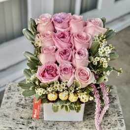 Pink roses arranged in a white square vase with small white filler flowers