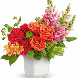 Mixed bouquet of orange roses, pink flowers, and green accents in a clear vase