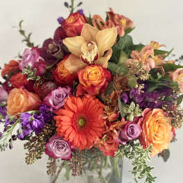 Mixed bouquet of roses, gerbera daisies, and orchids in a glass vase