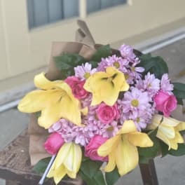 Bouquet of yellow lilies, pink roses, and lavender daisies wrapped in brown paper
