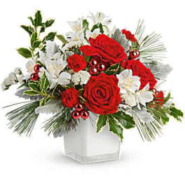 Red roses and white lilies in a white vase with holiday greenery
