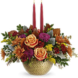 Floral centerpiece with two red taper candles in a gold vase