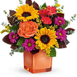 Mixed bouquet with sunflowers, roses, and daisies in an orange vase