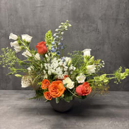 Mixed floral arrangement in a dark bowl vase with orange and white roses