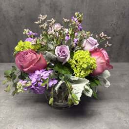 Pink and lavender roses arranged in a glass vase with purple blooms