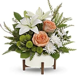 White lilies and peach roses in a white container with green accents